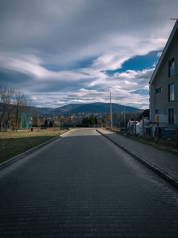 A serene view of a road leading towards mountains under a cloudy sky.