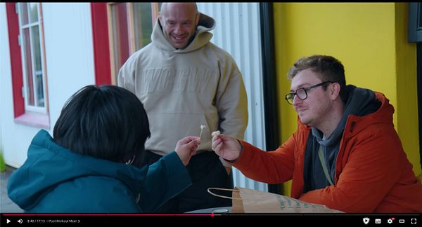 A group of three individuals is engaged in a lighthearted moment while preparing to taste fermented shark in Iceland.