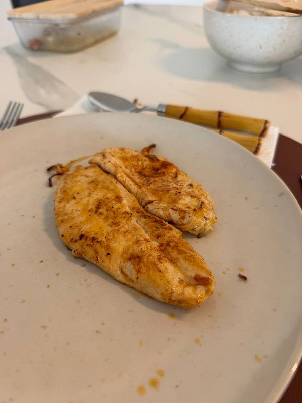 A close-up of a roasted chicken on a plate, garnished with lemon slices and herbs.