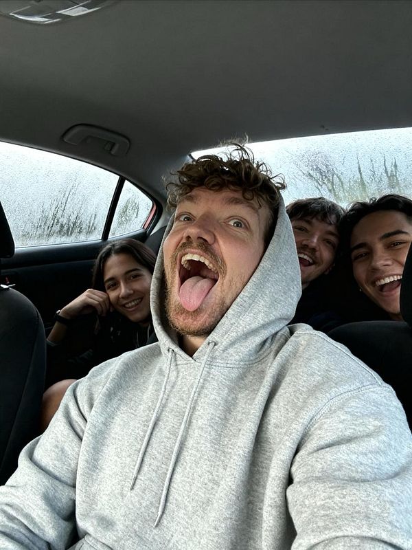 A group of four friends is having fun inside a car, with one person making a silly face.