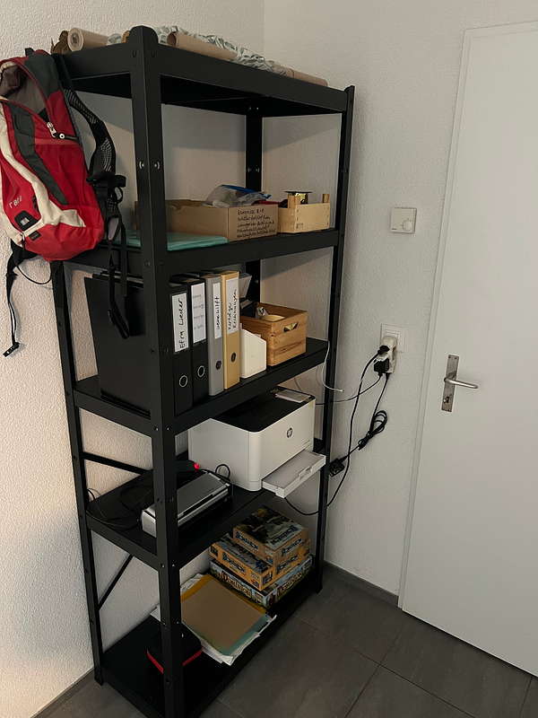 A black shelving unit is organized with various office supplies, a printer, and a scanner.