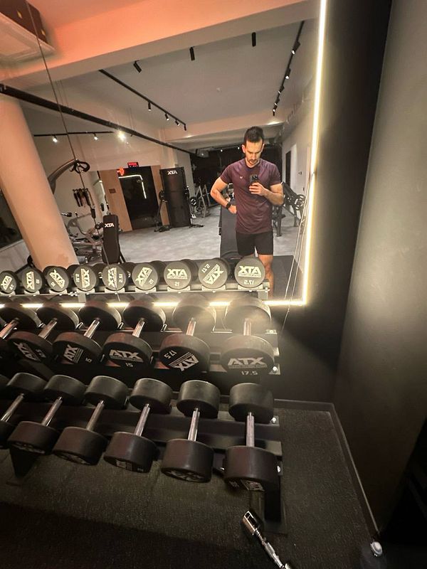 A gym setting featuring a person taking a selfie in front of a mirror with dumbbells in the foreground.
