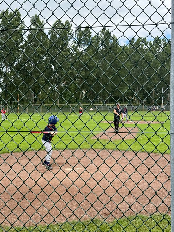 A young boy in a baseball uniform stands on the field, holding a bat, ready to bat, during his first baseball game.