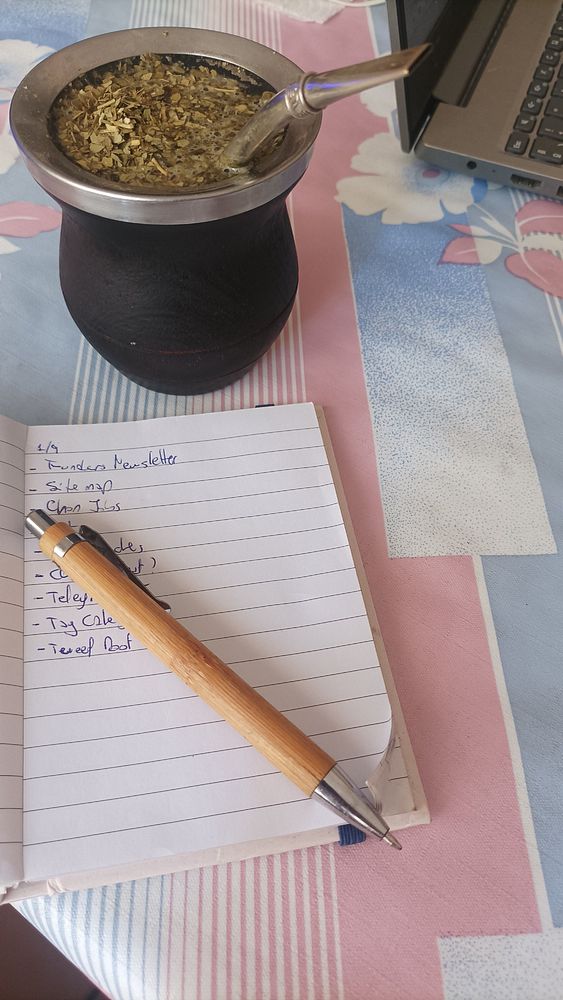 A workspace featuring a traditional mate drink, a notepad with tasks, and a laptop.