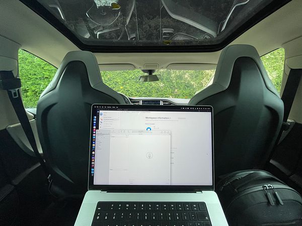 A workspace set up inside a Tesla vehicle with a laptop displaying a workspace information screen.