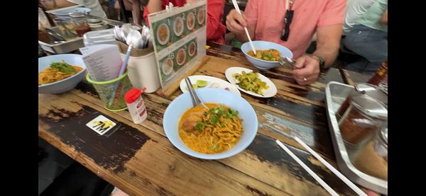 A bowl of Khao Soi featuring rich curry broth, meat, and noodles presented on a wooden table.