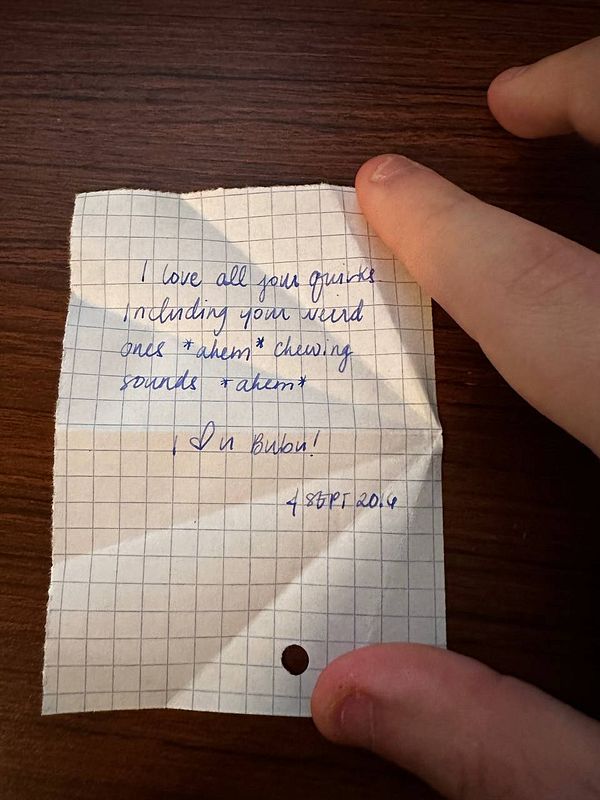 A handwritten love note on grid paper is being held by a person's hand.