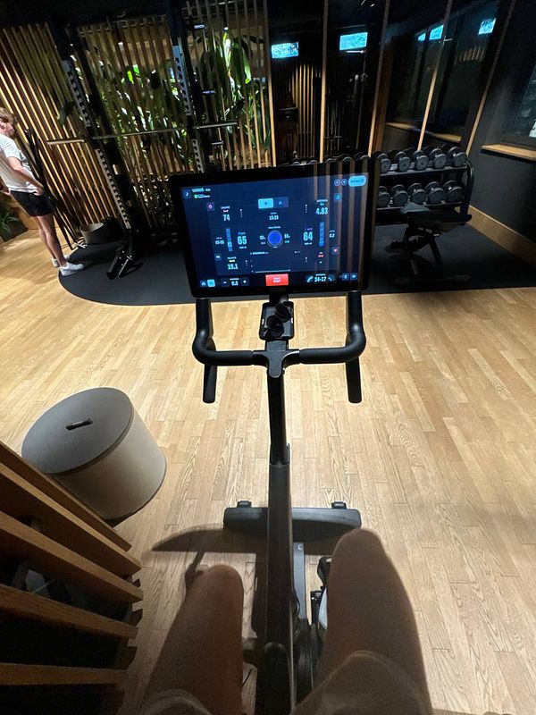 A person is seated on an exercise bike in a gym, with a digital display showing workout metrics.