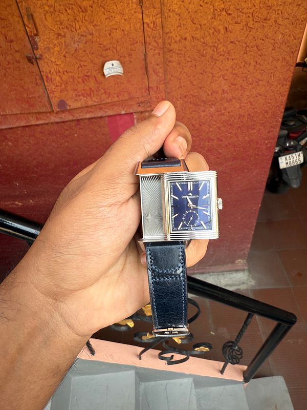 A hand holds a stylish watch against a textured background.