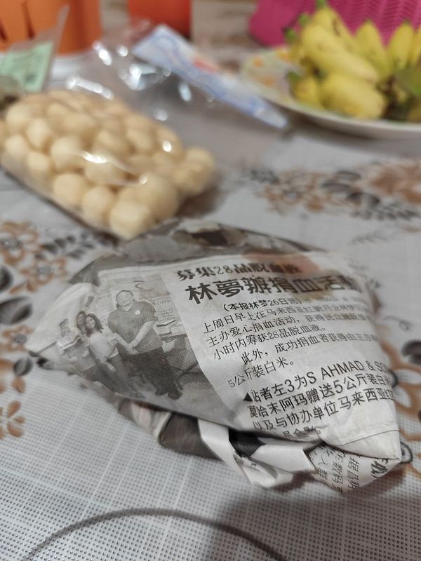 A classic fried kway teow wrapped in newspaper is placed on a table alongside other food items.