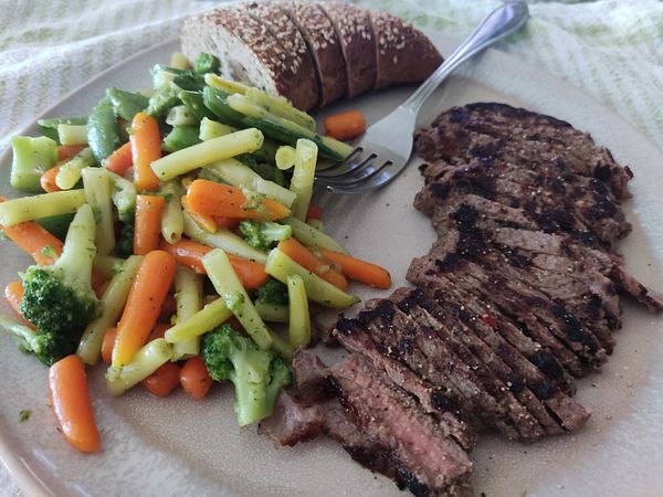 A plate featuring Croatian steak, mixed vegetables, and a slice of bread.