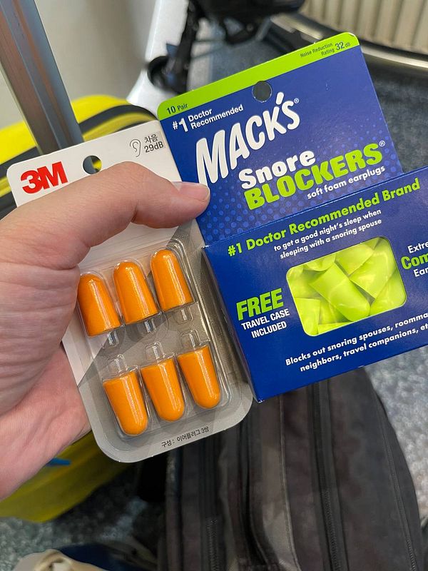 A hand holds two packages of earplugs from 3M and Macks.