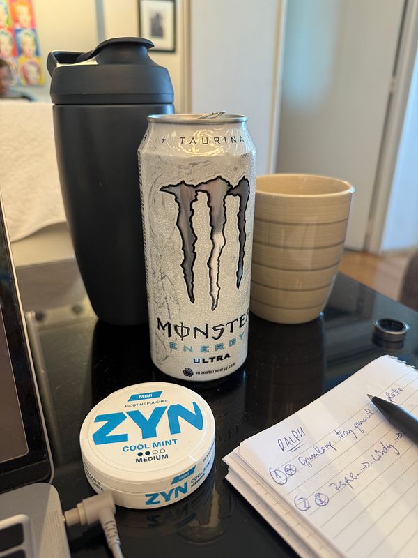 A workspace featuring energy drinks, nicotine pouches, and a notepad with tasks.