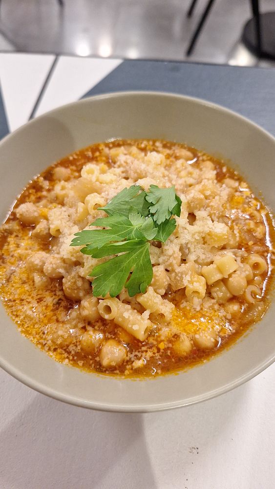 A bowl of pasta e ceci topped with cheese and fresh herbs.
