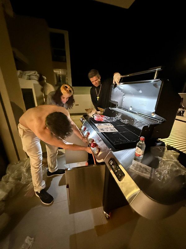 Three individuals are preparing a barbecue on a grill at night.