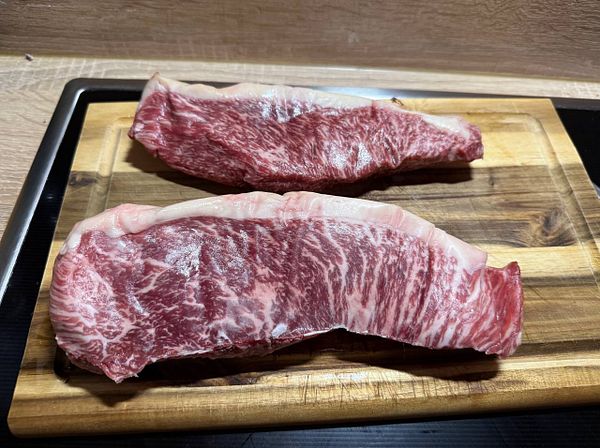 Two pieces of marbled steak are displayed on a wooden cutting board.