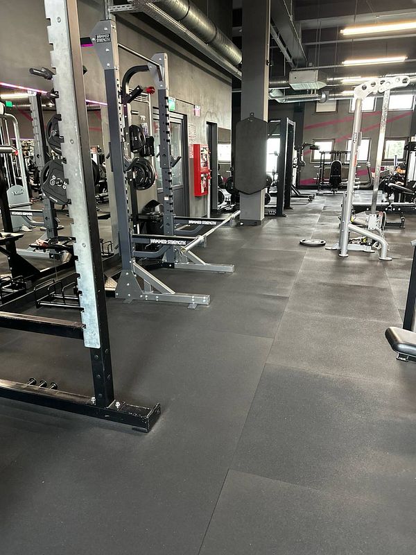 The image depicts a well-equipped gym interior featuring various strength training equipment.