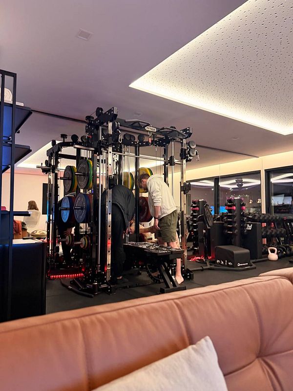 Two people working out on gym equipment in a modern fitness space with a brown couch in the foreground.