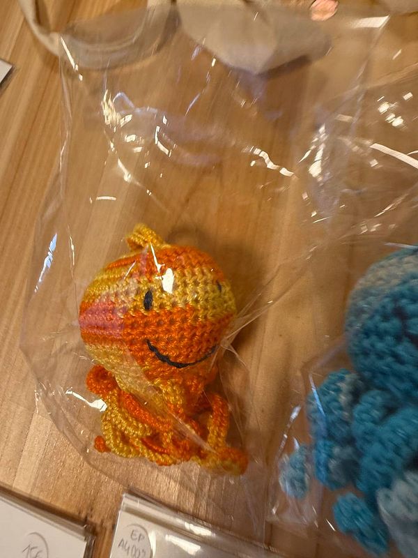 A colorful crocheted octopus toy is displayed in a plastic bag on a wooden surface.