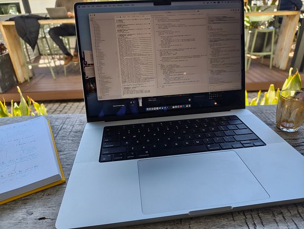 A laptop is open on a wooden table, displaying a code editor with information about stellar variability, alongside a notebook and a glass.