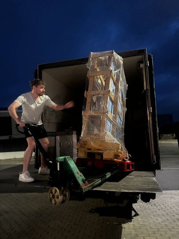 A man is unloading a large, wrapped stone table from a truck using a pallet jack.