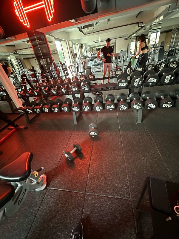 A gym interior featuring dumbbells, exercise equipment, and two individuals.