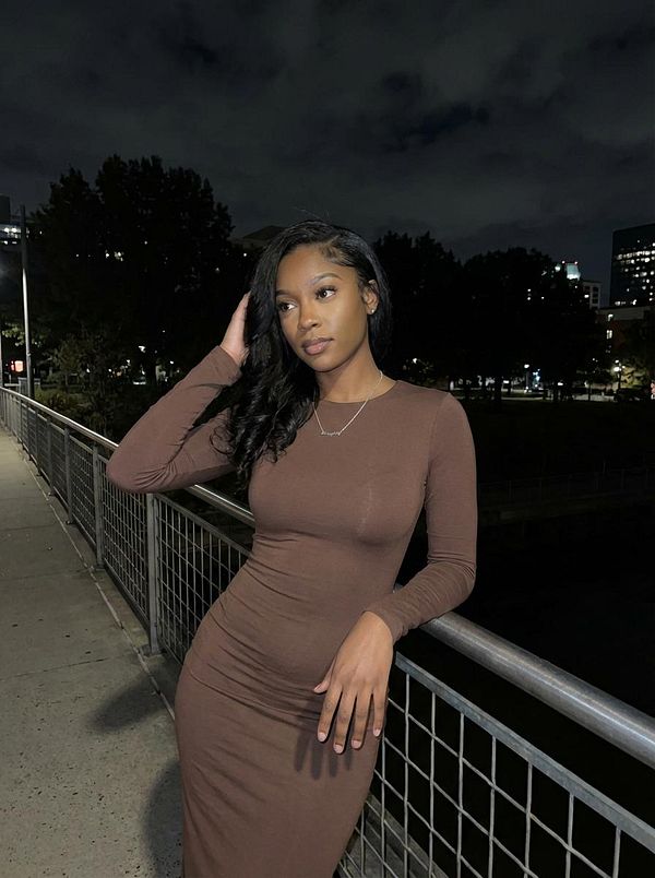 A woman poses elegantly at night on a bridge with city lights in the background.