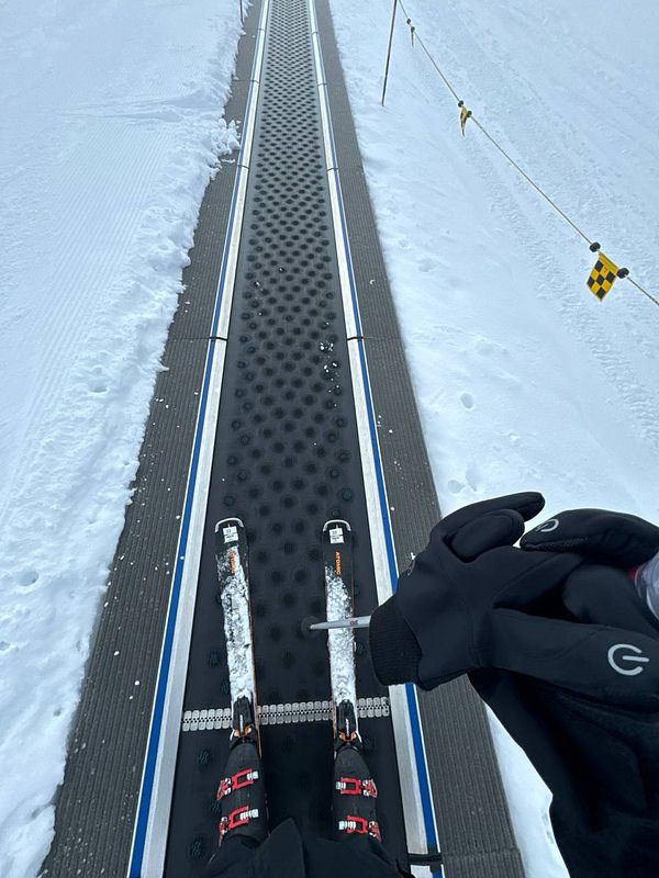 A skier stands on a conveyor belt at a ski resort, ready to ascend a slope.