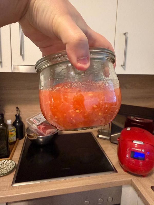 Close-up view of a jar of tomato puree in a gray ceramic bowl, ready for use in making Pa amb tomàquet.