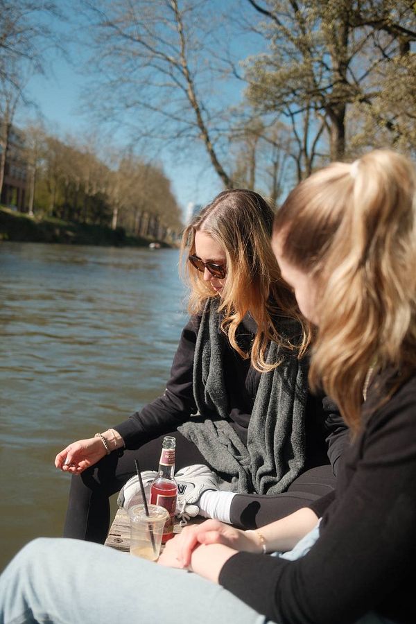 Two young women relax by a river on a sunny day.