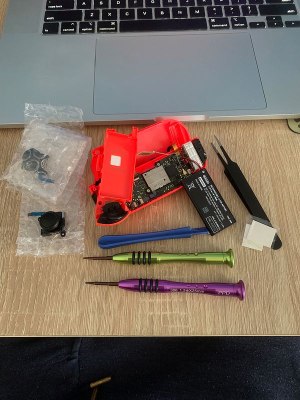 The image displays disassembled Nintendo Switch Joy-Con components alongside various tools and parts on a wooden surface.