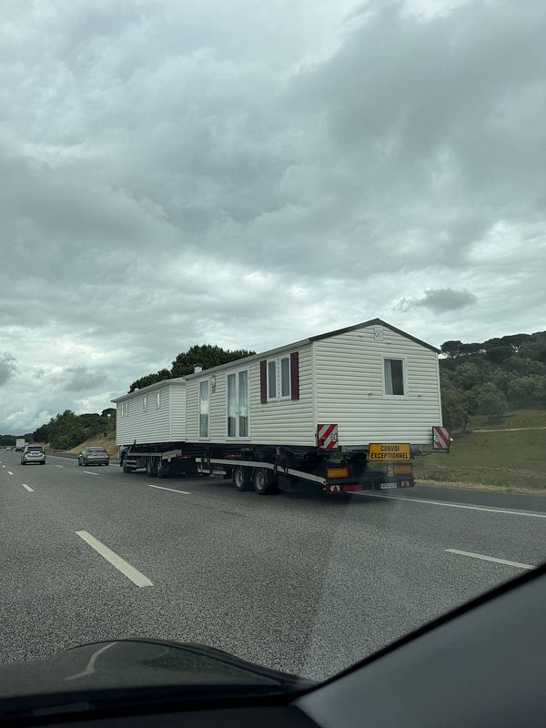 A small house mounted on a trailer is being towed by a vehicle on a Portuguese highway.