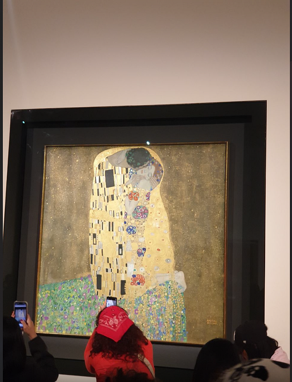 Visitors admire Gustav Klimt's iconic painting 'The Kiss' in a gallery setting.