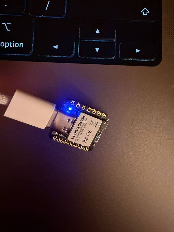 A close-up image of a Xiao NRF52840 microcontroller connected to a laptop via USB.