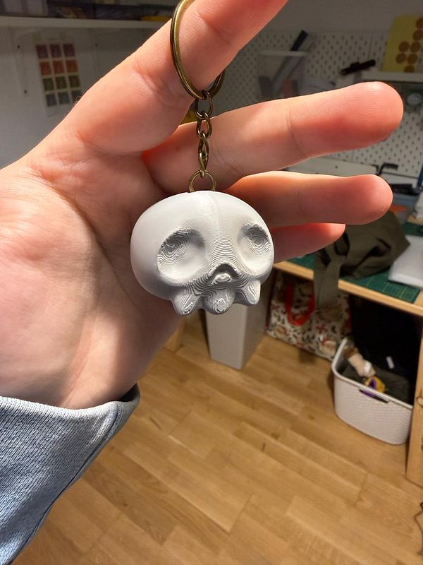 A hand holds a unique keychain shaped like a stylized skull.
