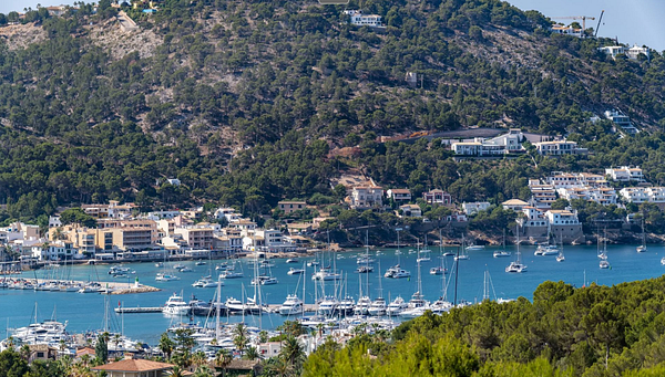 A picturesque coastal view featuring a marina filled with yachts and villas on the hillside.