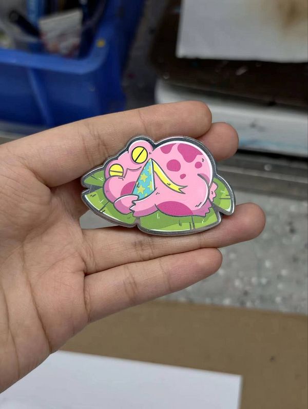 Close-up photo of four enamel pins featuring various colorful and playful designs laid out on a white surface.