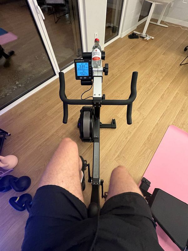 A person is seated on a rowing machine in a home gym setting.