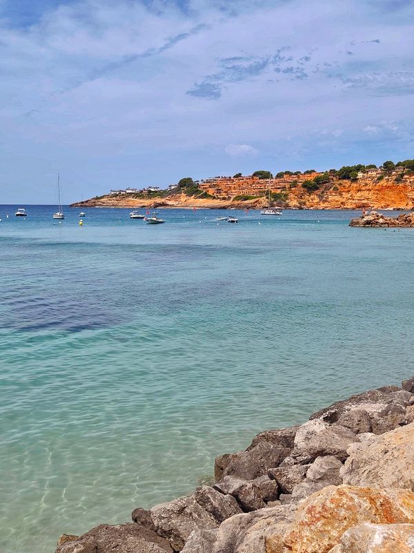 Scenic coastal cliffside landscape with clear blue water and a bright sky.