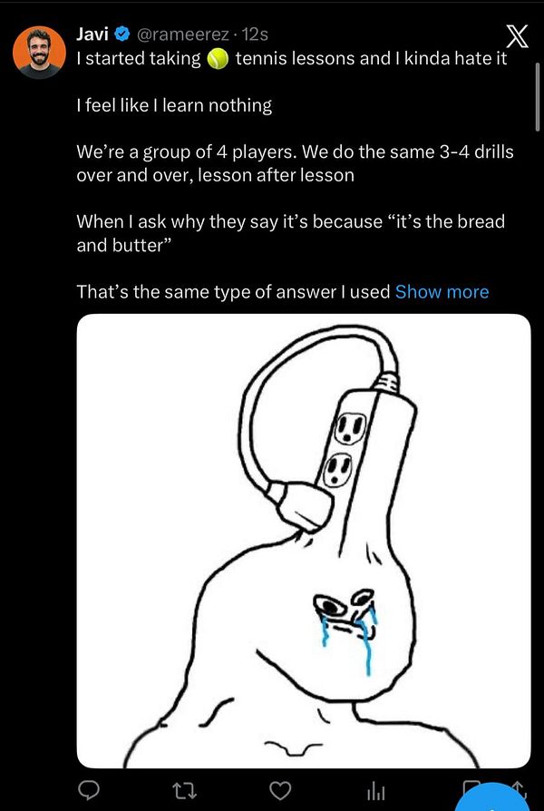 A man holding a tennis racket, standing on a tennis court, smiling at the camera, with another person in the background playing tennis.