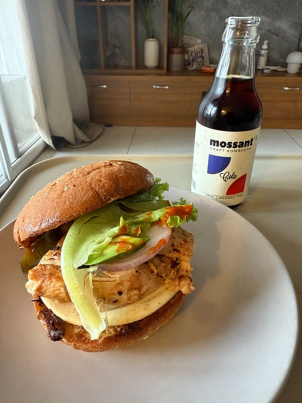 A delicious chicken sandwich served with a bottle of kombucha.