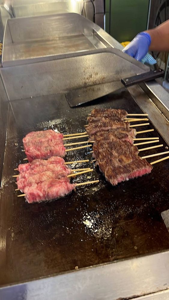 Wagyu beef skewers are being grilled on a hot surface.