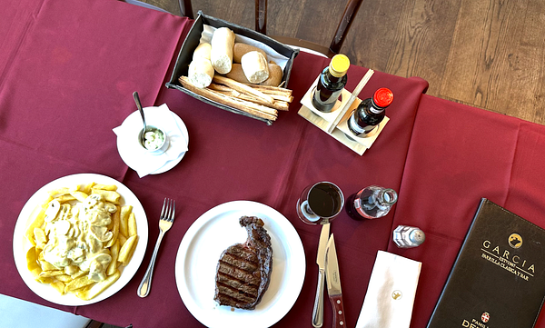 A dining table set with a plate of fries, a steak, and various condiments.