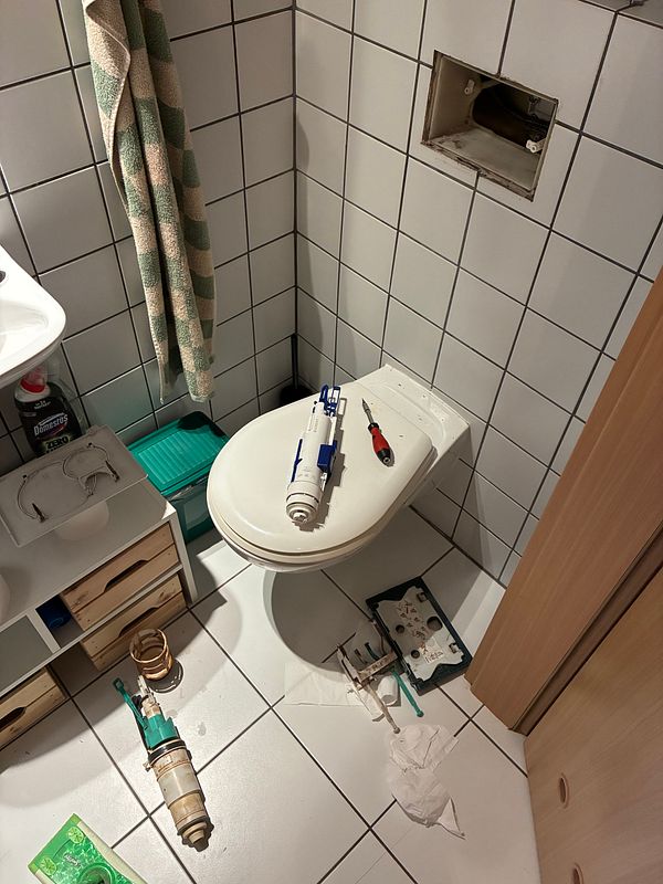 Black and white photo of a man repairing or inspecting the base of a residential toilet in a bathroom.