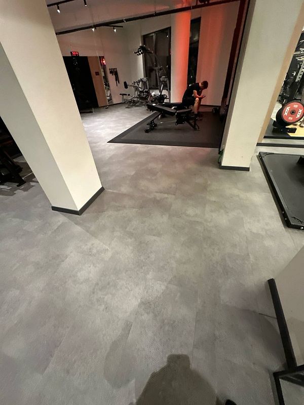 A dimly lit gym interior featuring workout equipment and a person resting on a bench.