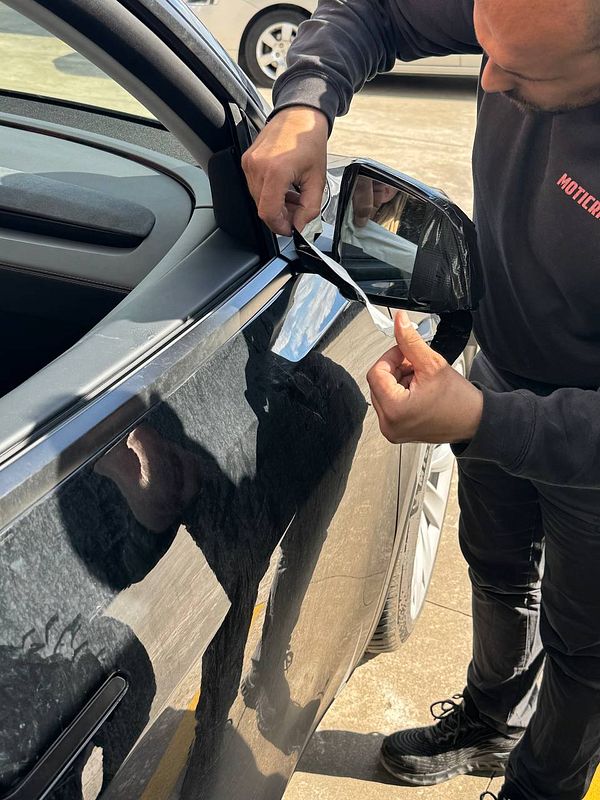 A mechanic is repairing a car's side mirror at a mechanic shop.