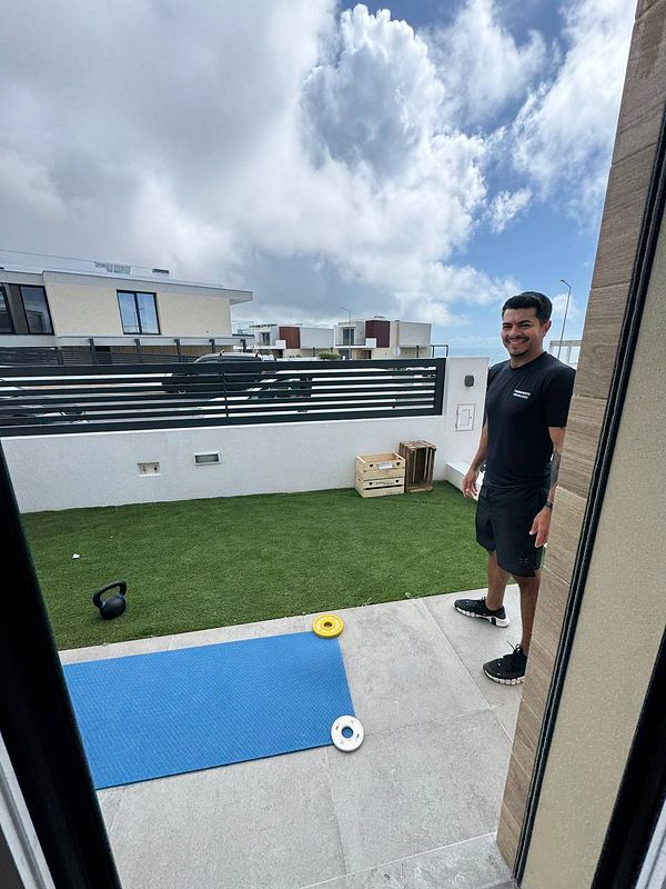 A personal trainer stands outside in a home gym setting, ready for a workout session.