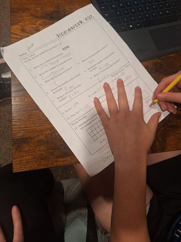 A child is working on a 4th grade math homework sheet while seated at a table.