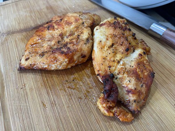 Grilled chicken breasts are displayed on a wooden cutting board.