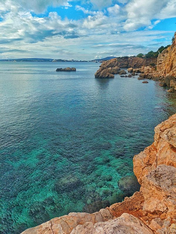 A scenic coastal view featuring rocky cliffs and clear turquoise waters.
